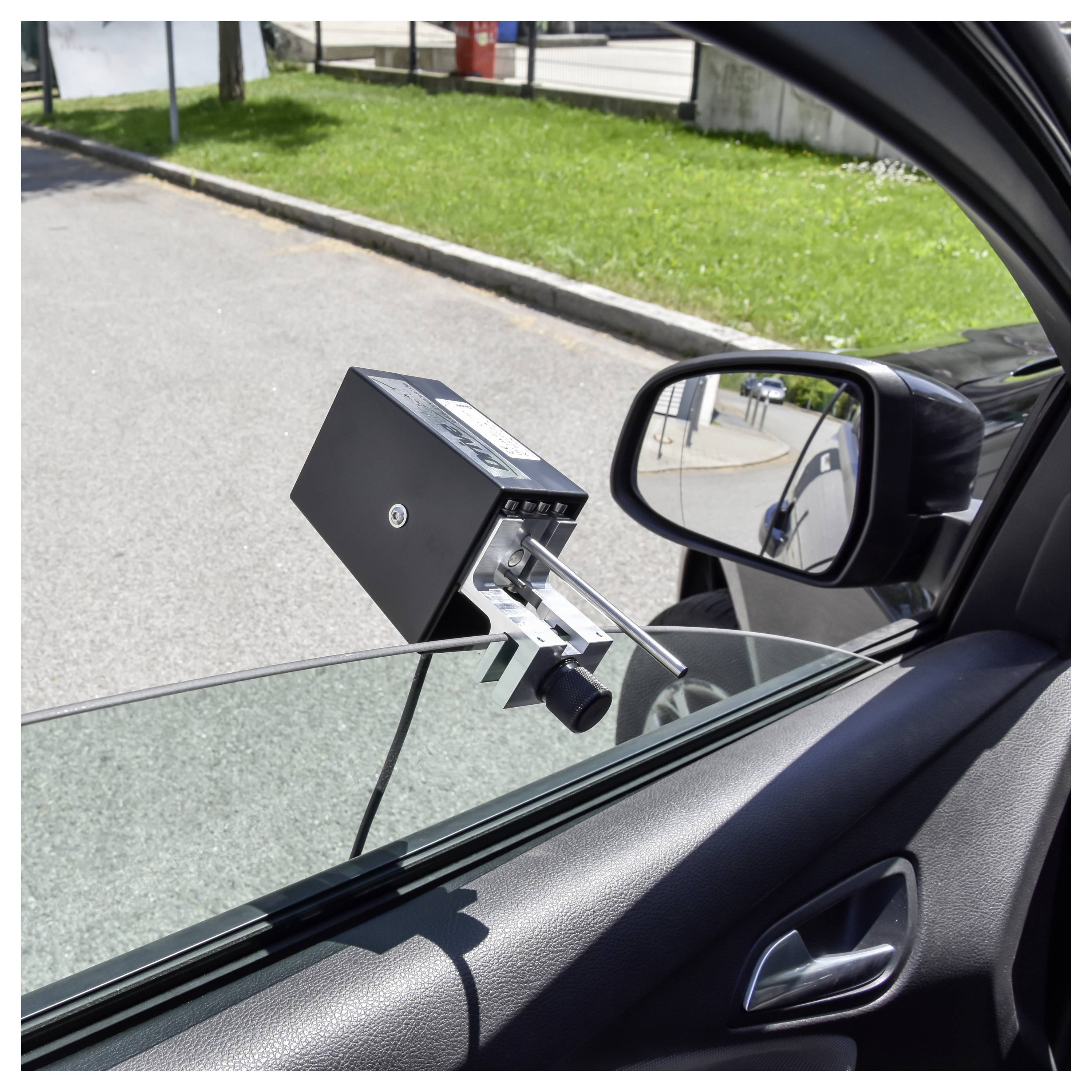 Ein am Auto montiertes Gerät ist außen am offenen Vorderfenster befestigt, mit einer kleinen kameraähnlichen Einheit, die sich zur Straße erstreckt.