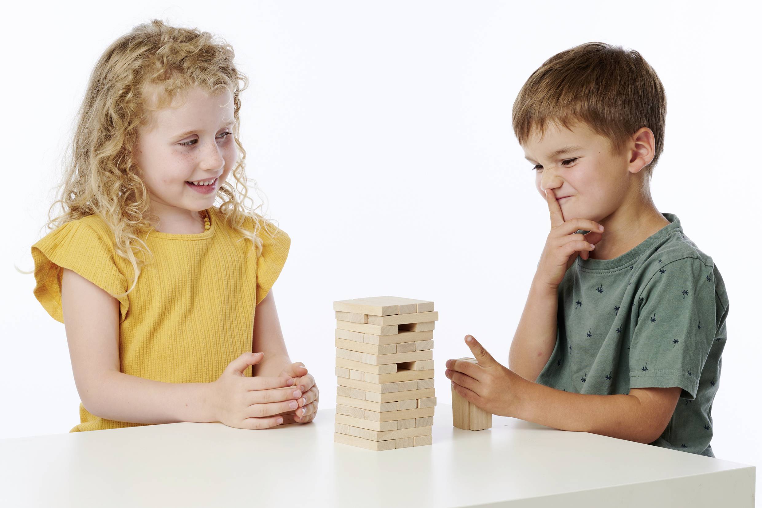 Zwei Kinder spielen am Tisch mit einem Jenga-Turm aus Holzklötzen. Das Mädchen lacht, während der Junge konzentriert überlegt.