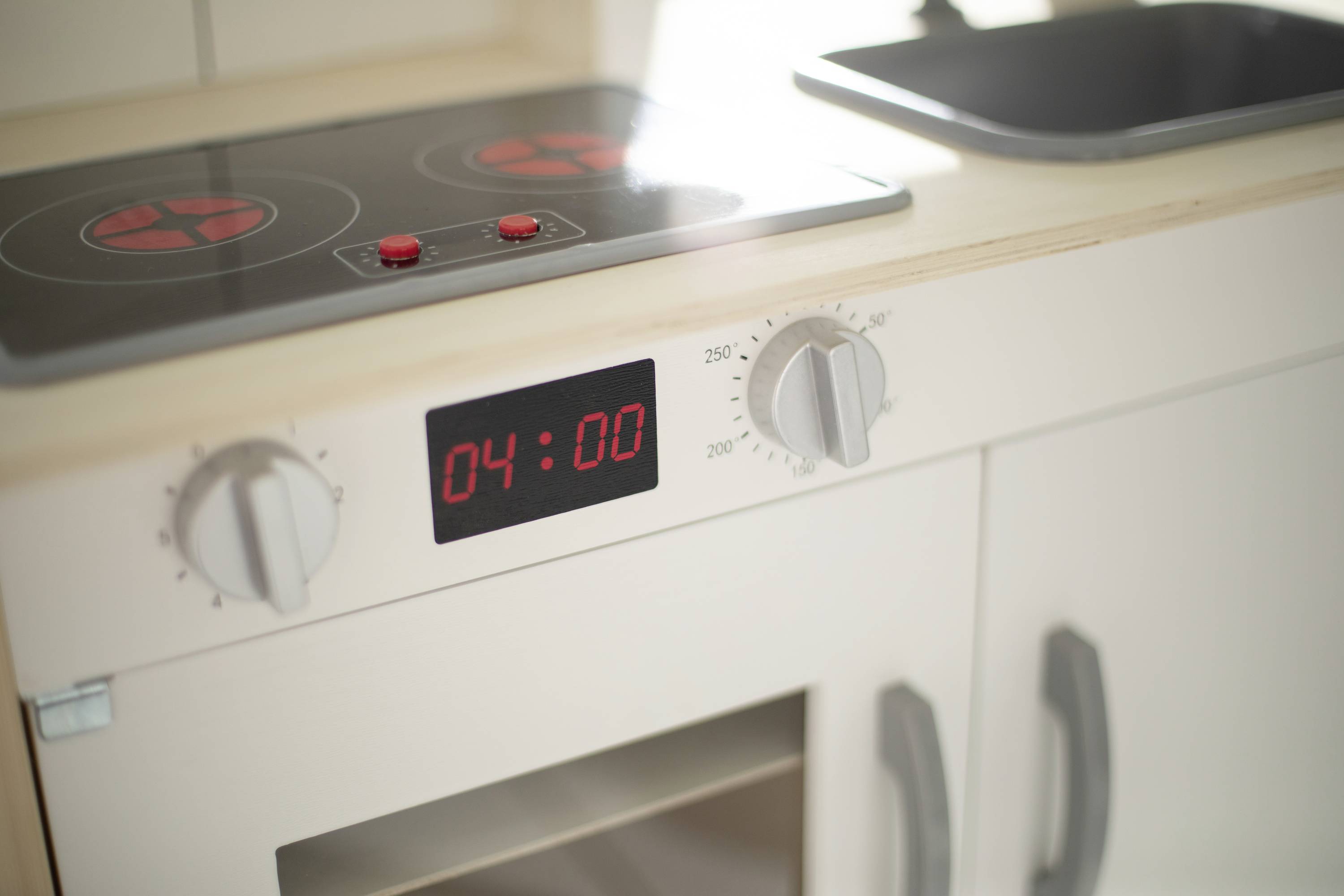 Elektrischer Herd mit digitaler Anzeige zeigt '04:00', Temperaturregler auf 250 Grad, eingebaut in eine weiße Küchenzeile.