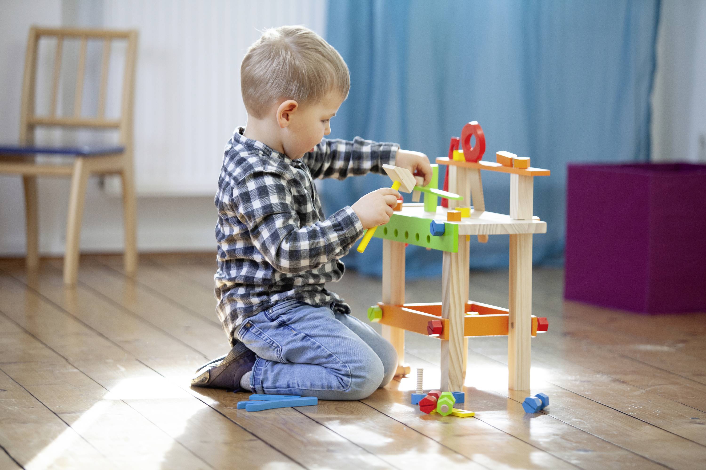Kleiner Junge spielt konzentriert auf Holzboden mit buntem Werkzeugspielset.