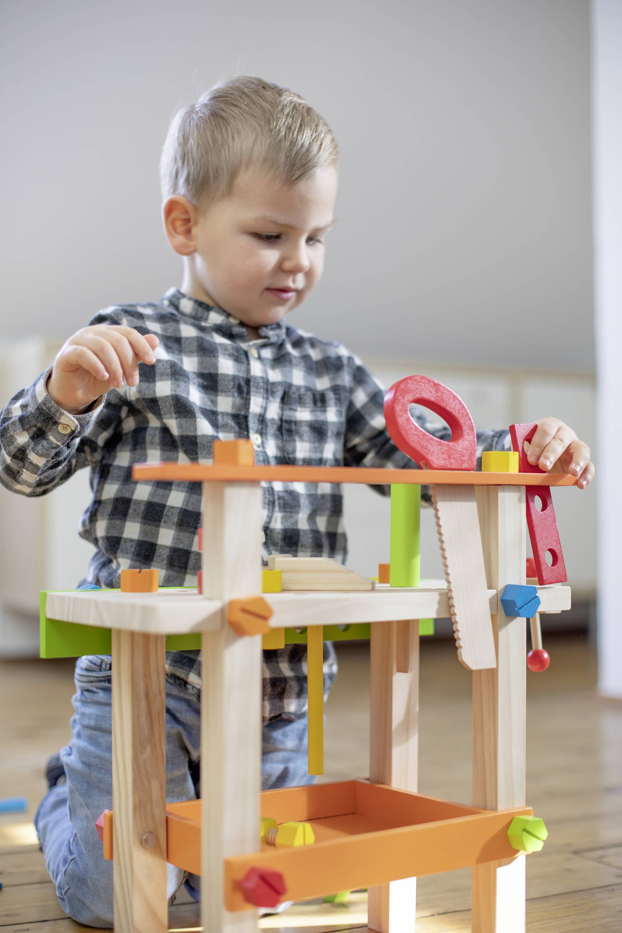 Ein kleiner Junge spielt mit einem bunten Holzbaukasten im Wohnzimmer. Er konzentriert sich auf seine Konstruktion aus Holzteilen.