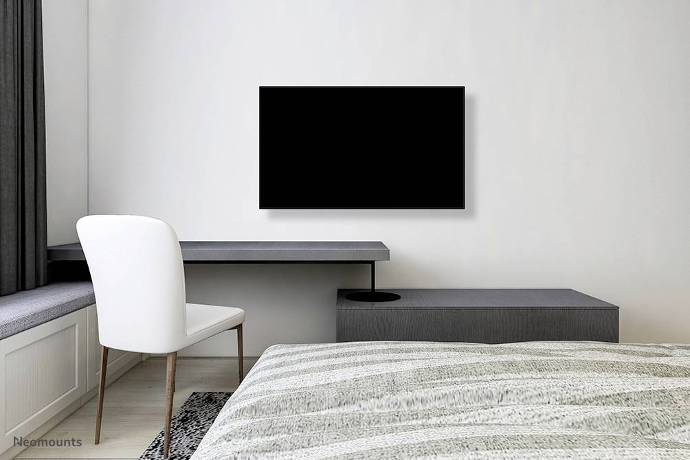 Ein modernes Schlafzimmer mit einem grauen Schreibtisch, einem weißen Stuhl und einem großen Flachbildfernseher an der Wand.