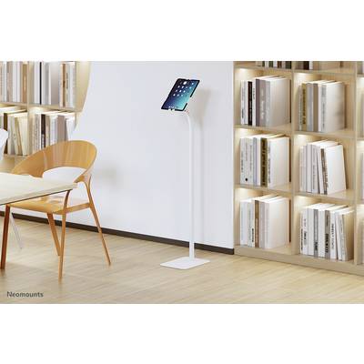 Ein Tablet steht auf einem weißen Ständer neben einem leeren orangefarbenen Stuhl vor Regalen mit Büchern in einem modernen Raum.