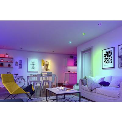 Wohnzimmer mit Sofa, Tisch und farbiger Beleuchtung. Dekorative Bilder an der Wand, Fahrrad an der Ecke und offene Küche im Hintergrund.