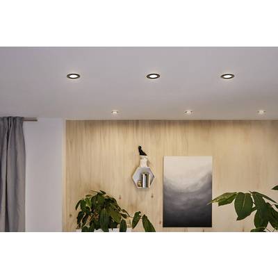 Ein Wohnzimmer mit Holzvertäfelung, mehreren Topfpflanzen und einem modernen Gemälde. Kleine Deckenlampen beleuchten den Raum.