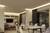 Modernes Wohnzimmer mit eleganter Beleuchtung, Esstisch und Stühlen. Im Hintergrund ein Fernseher und Sofa, wohnliche Atmosphäre.