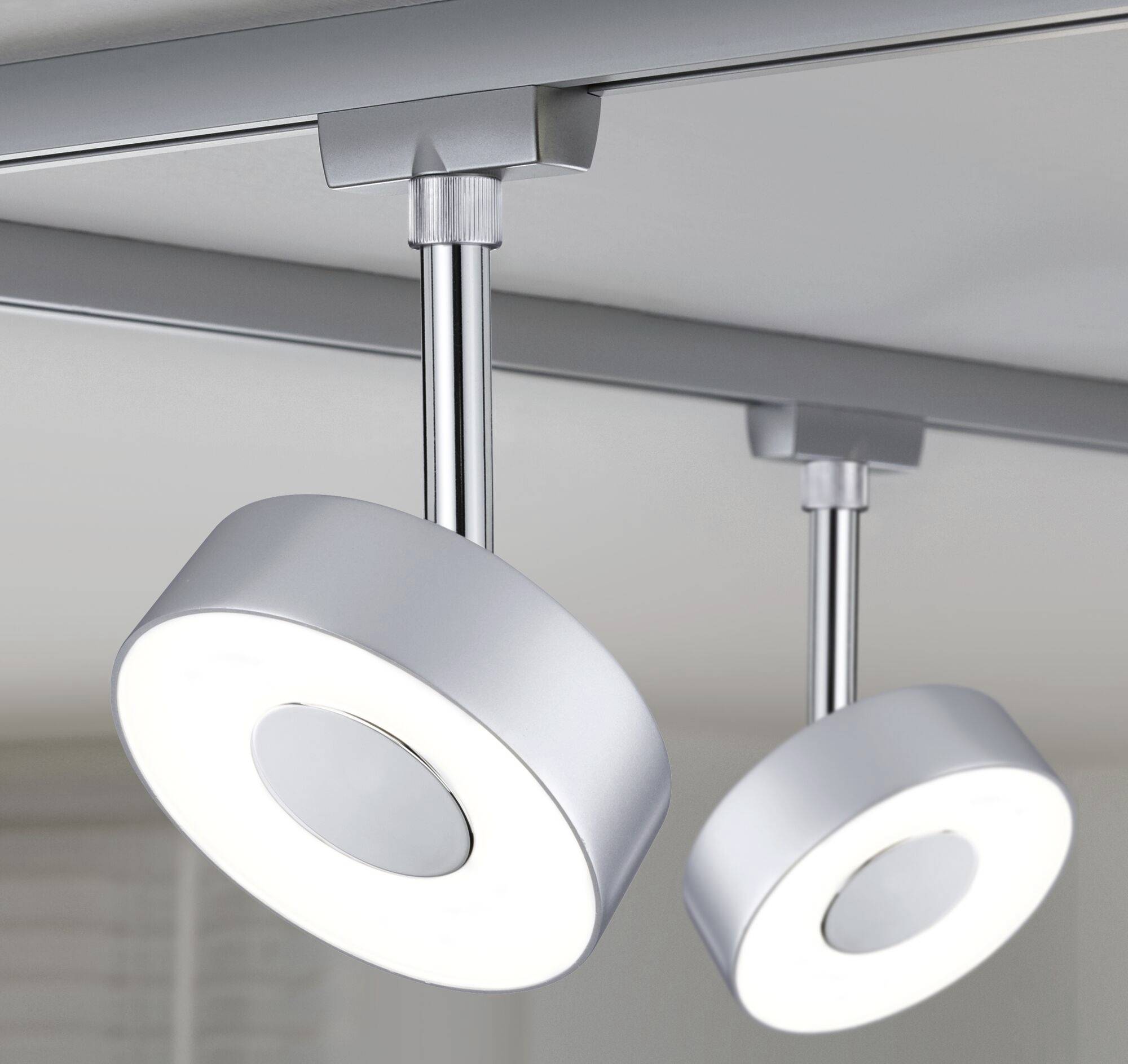 Zwei moderne LED-Deckenleuchten mit rundem, silberfarbenem Design. Sie sind an einer weißen Schiene montiert und beleuchten einen Raum.