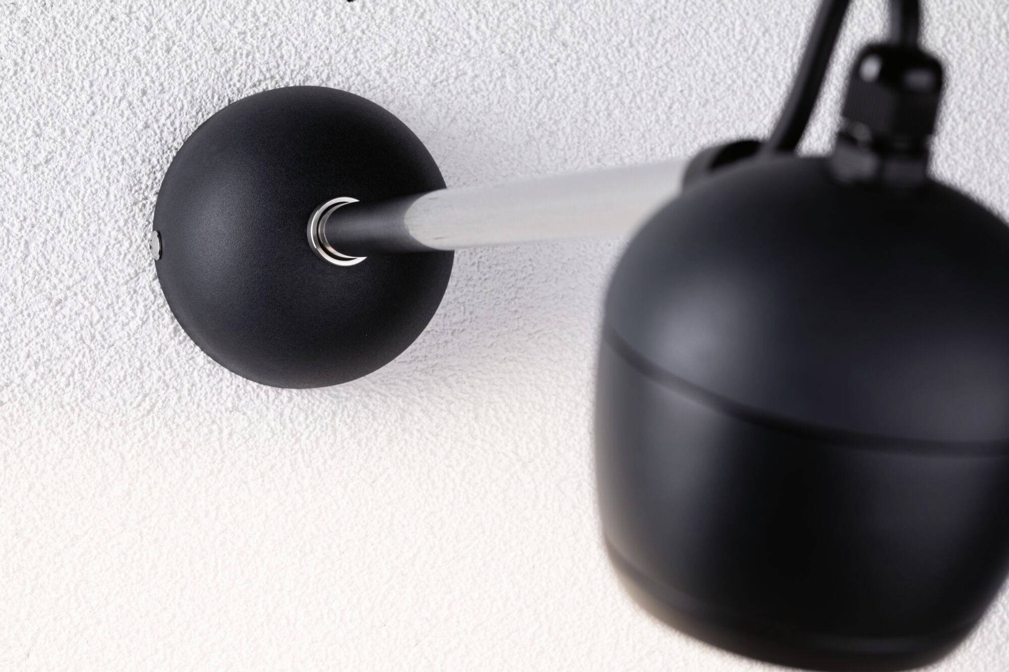 Überwachungskamera an der Decke montiert, zeigt nach unten, Fokus auf Kamera und Halterung vor strukturiertem Hintergrund.
