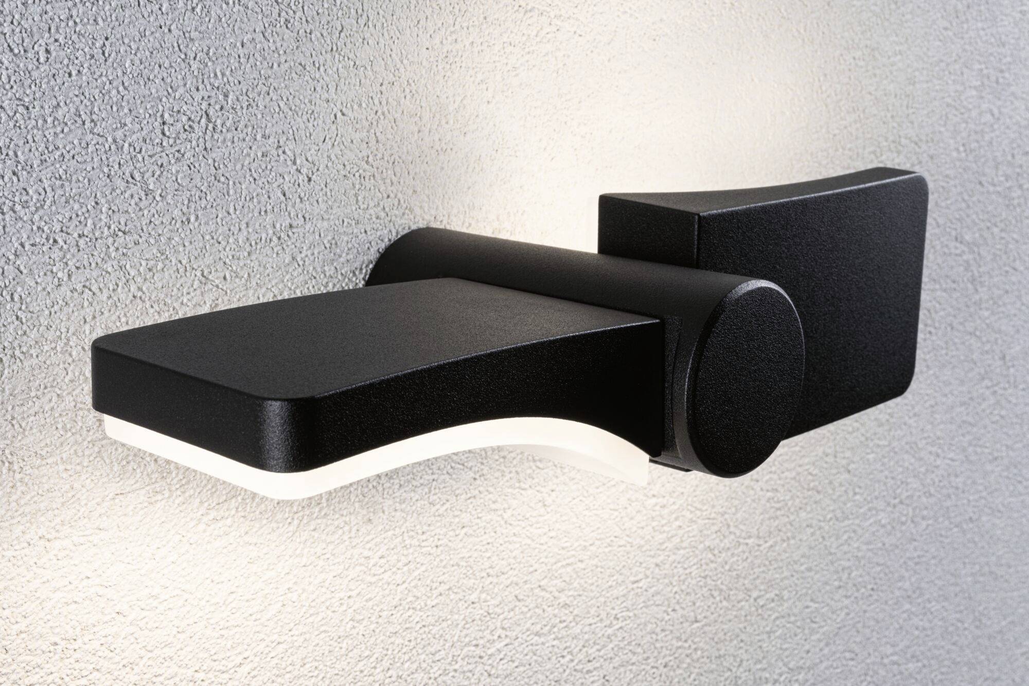 Schwarze, moderne Wandlampe mit geschwungener Form, leuchtet warmweiß auf strukturiertem, grauen Hintergrund.