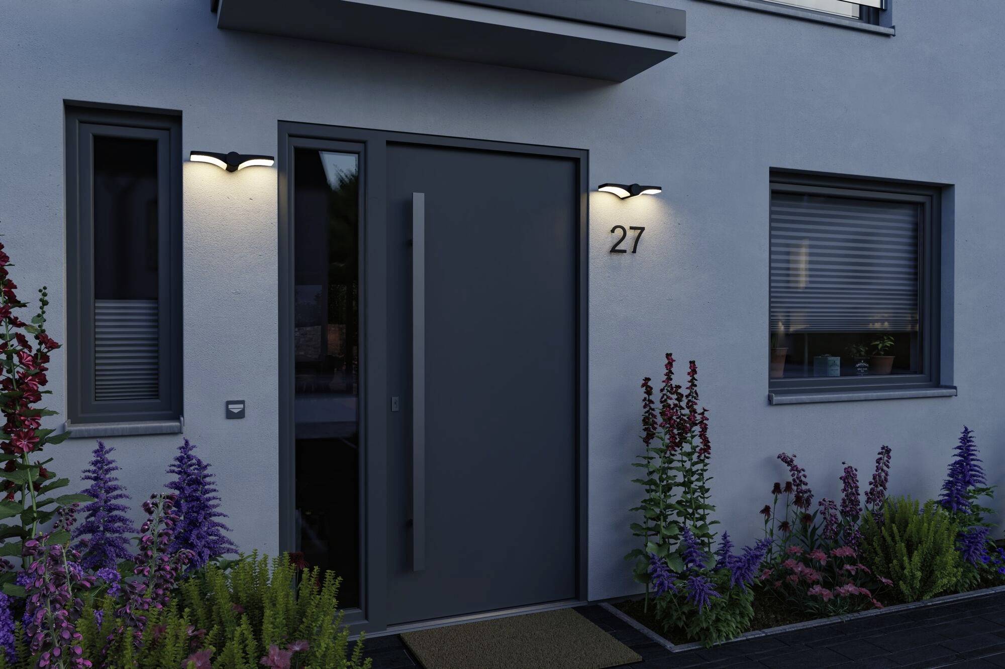 Eingang eines modernen Hauses bei Dämmerung, mit Tür unter Beleuchtung, umgeben von Blumenbeeten und der Hausnummer 27 sichtbar.