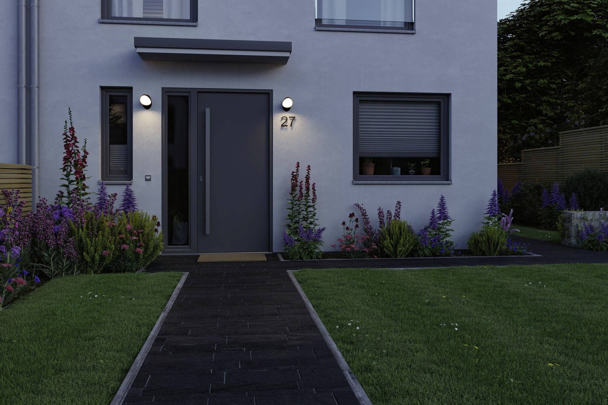 Eingang eines modernen Hauses mit grauer Tür, flankiert von Blumenbeeten und beleuchtet durch zwei runde Außenleuchten.