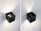 Zwei schwarze, würfelförmige Außenleuchten an einer Wand. Die linke leuchtet stärker nach oben und unten, die rechte weniger intensiv.