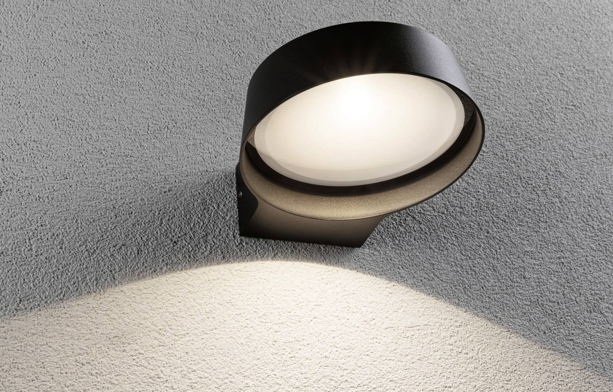 Eine moderne, schwarze Außenleuchte an einer grauen Wand, die nach unten gerichtet leuchtet und weiches Licht auf die Oberfläche wirft.