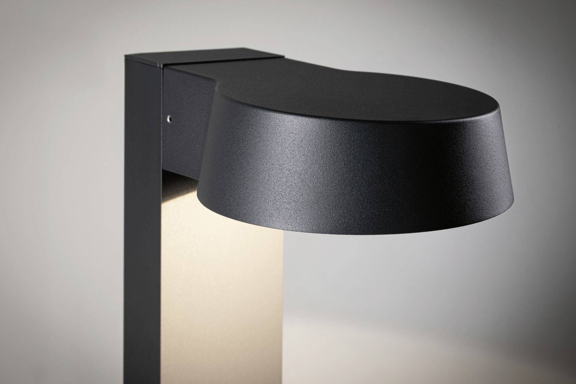 Moderne, schwarze Außenleuchte mit eckigem Sockel und rundem Schirm, beleuchtet Umgebung mit indirektem Licht.