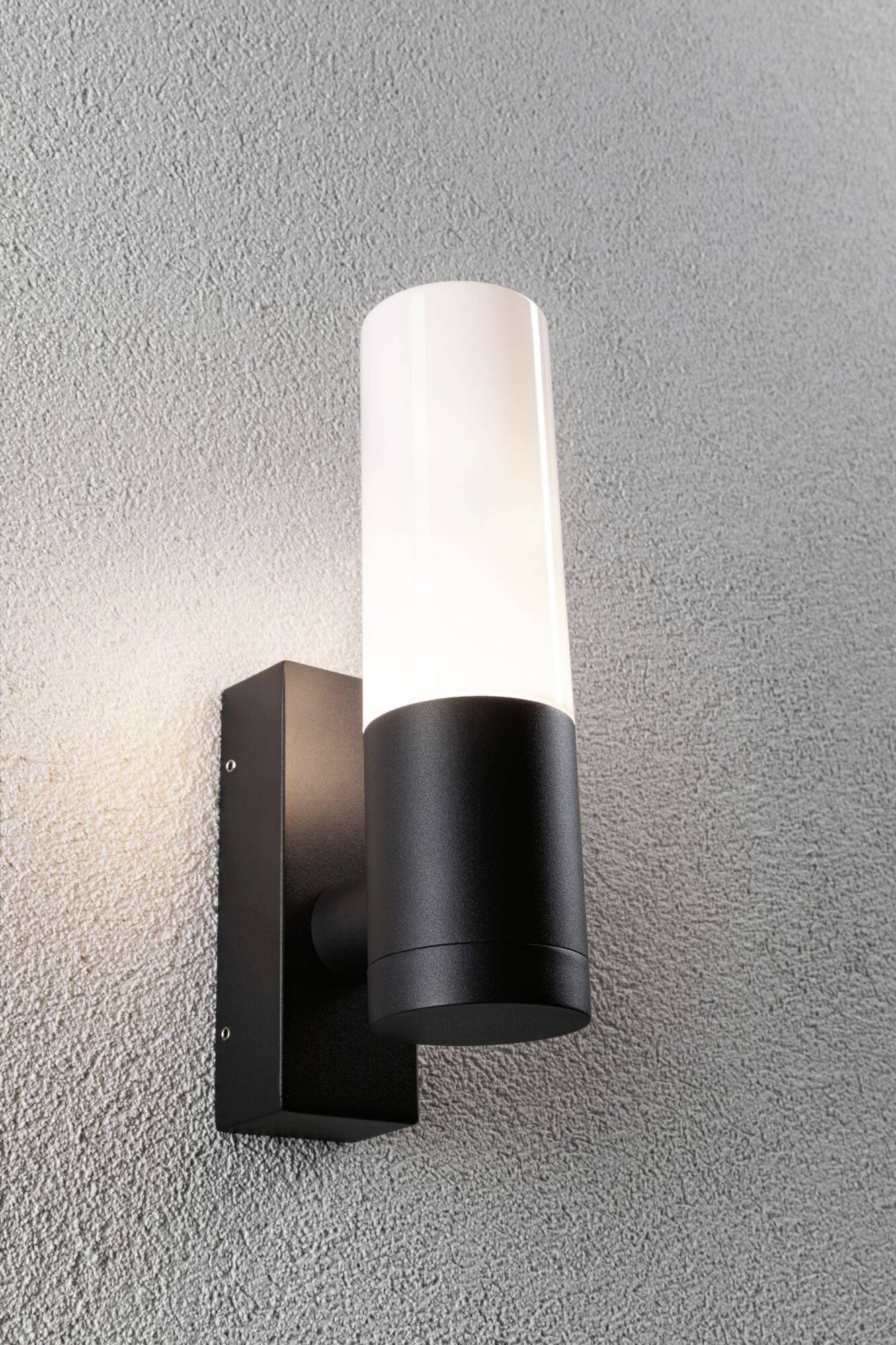 Wandleuchte mit modernem, zylindrischem Design; schwarzes Gehäuse mit weißem, leuchtendem Diffusor. Befestigt an grauer Wand.