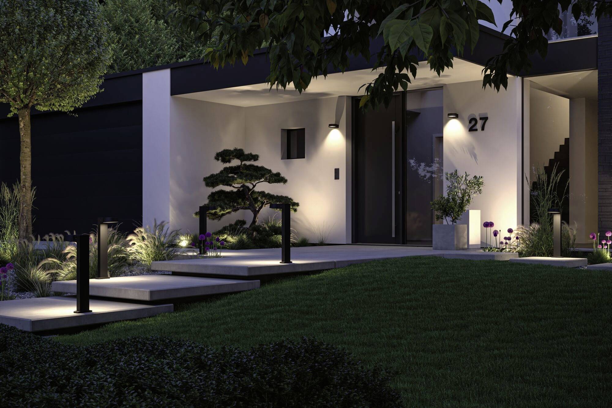 Ein modern beleuchtetes Haus mit Weg und Garten bei Nacht. Hausnummer '27' an der Fassade sichtbar, umgeben von Pflanzen und Rasenflächen.