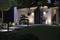 Moderne Hausfassade bei Nacht mit beleuchteten Wegen und gepflegtem Garten.