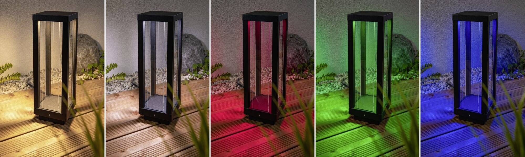 Fünf Laternen, jede leuchtet in einer anderen Farbe: gelb, rot, grün, blau, violett, auf einer Holzterrasse neben Pflanzen.