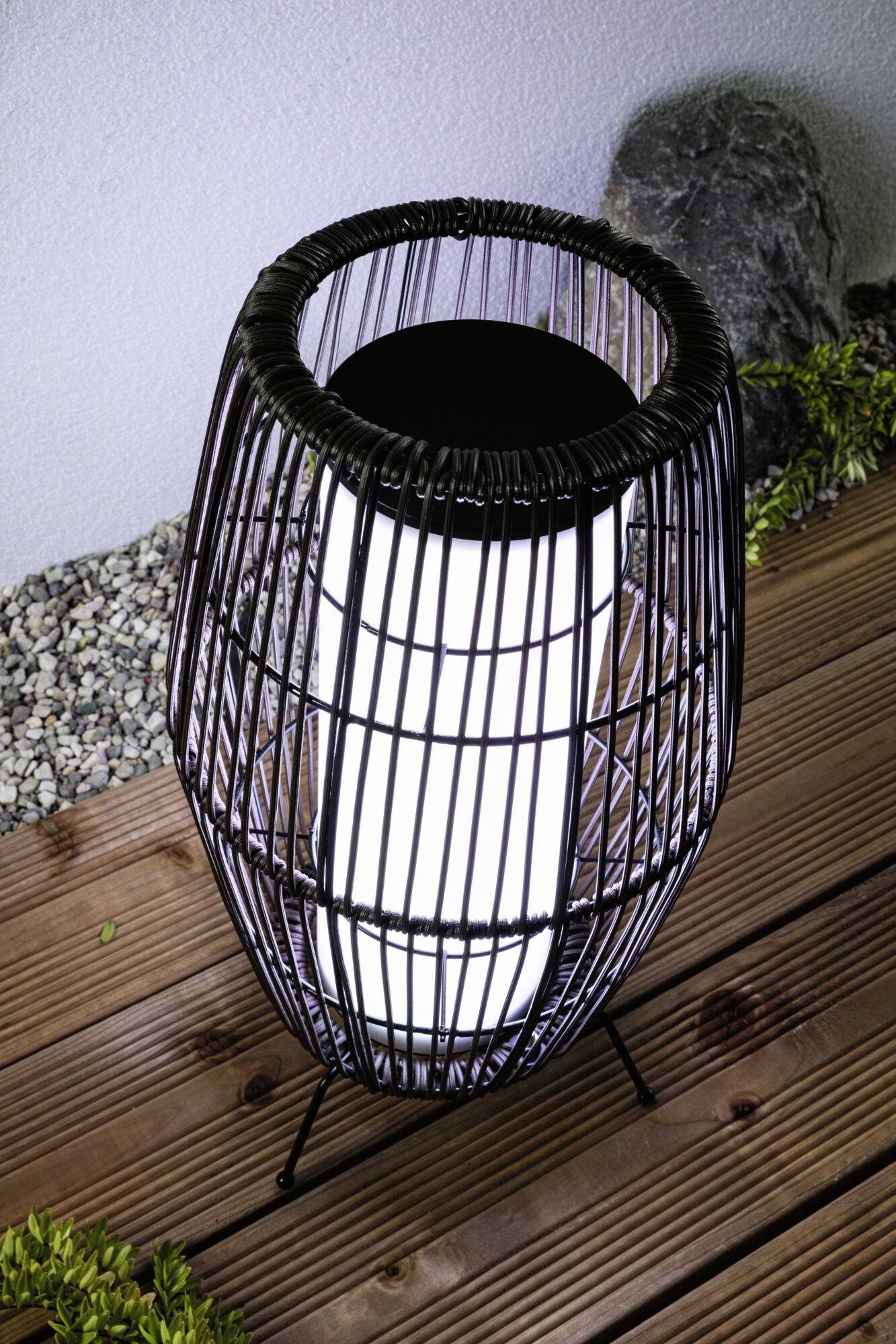 Eine moderne Bodenlampe mit schwarzem Drahtgestell beleuchtet hölzerne Terrassendielen. Im Hintergrund liegen weiße Kieselsteine.