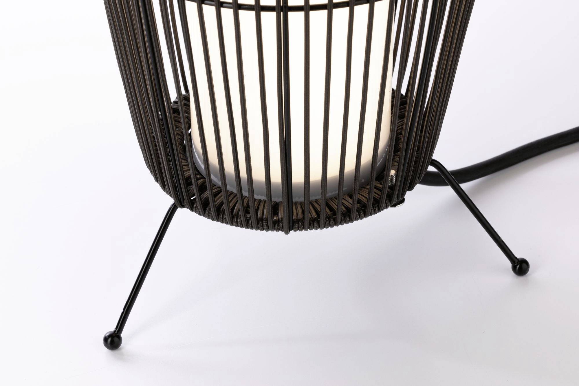 Eine stilvolle Lampe mit einem offenen, korbförmigen Metallrahmen. Sie strahlt warmes Licht aus und steht auf drei schlanken Beinen.