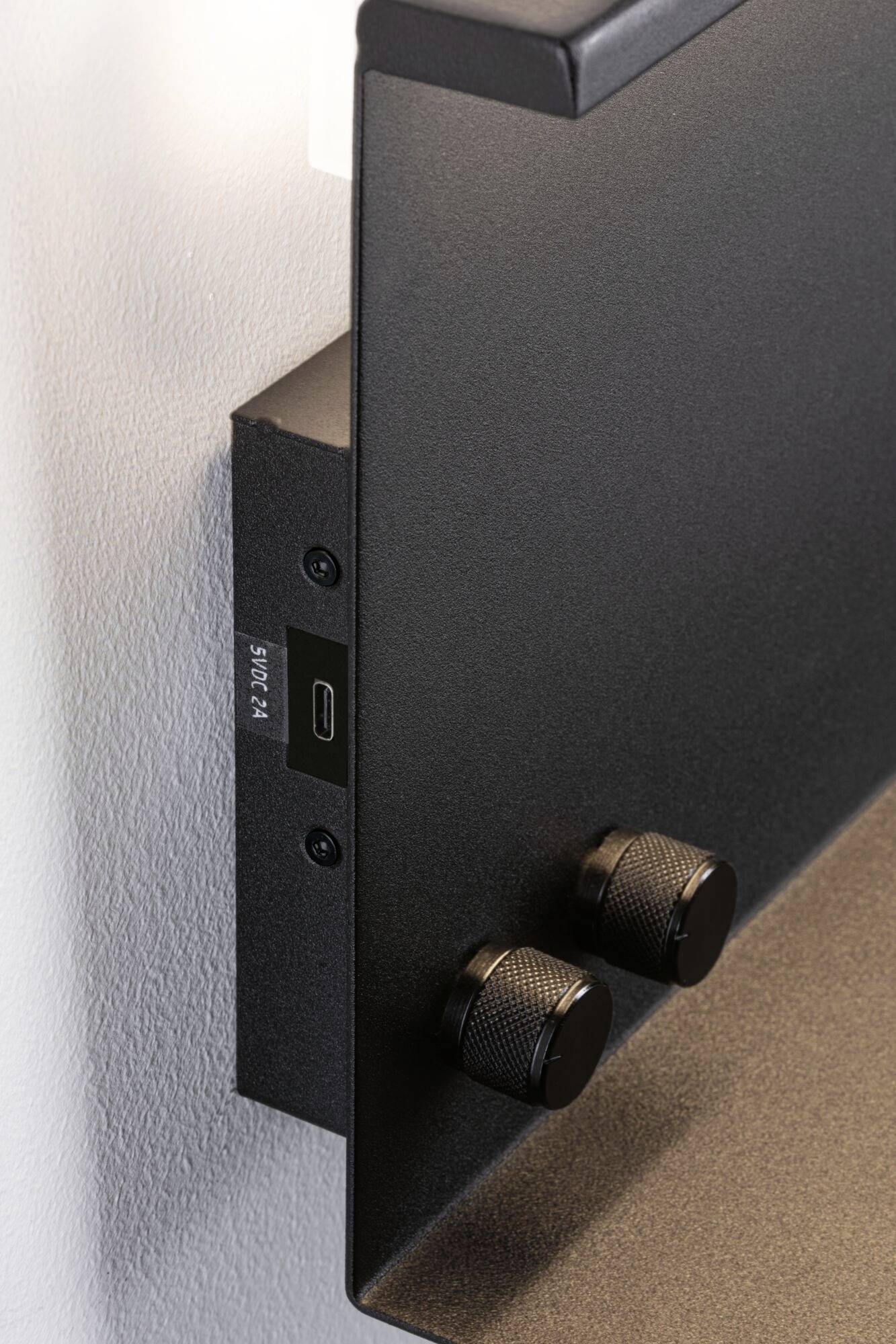 Ein schwarzer Lautsprecher an der Wand mit USB-C-Anschluss und zwei Drehknöpfen an der Seite.