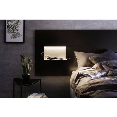 Ein gemütlich eingerichtetes Schlafzimmer mit Bett, darüber ein Regalbrett mit Beleuchtung. Ein Kaktus steht auf einem kleinen Tisch.