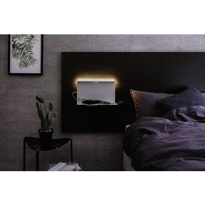 Ein beleuchtetes Wandregal neben einem Bett in einem modernen Schlafzimmer, dekoriert mit einem Kaktus und gerahmtem Pflanzenbild.
