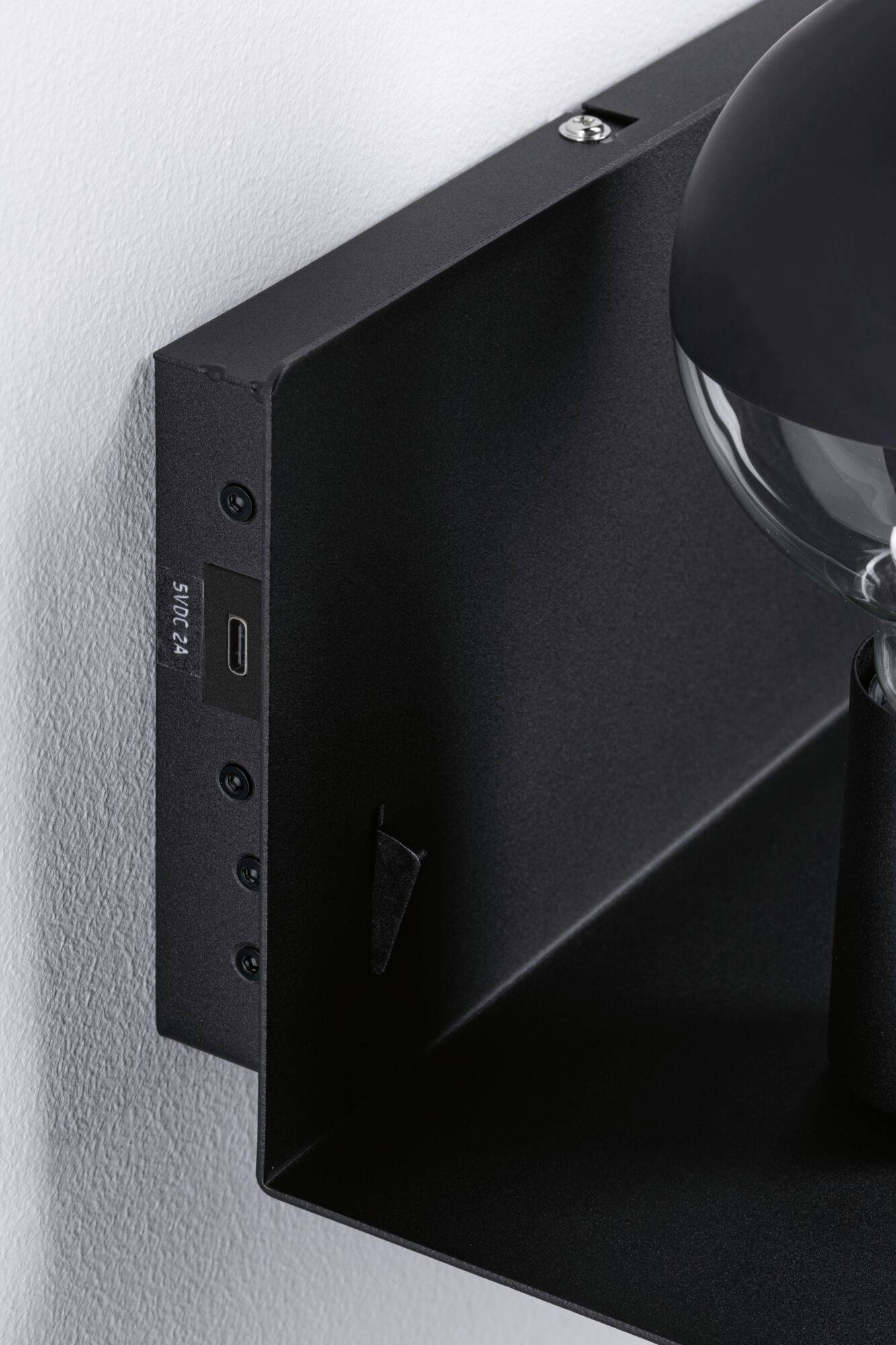 Eine schwarze Wandlampe mit integriertem USB-Anschluss und Ein/Aus-Schalter. Die Lampe ist an einer weißen Wand montiert.