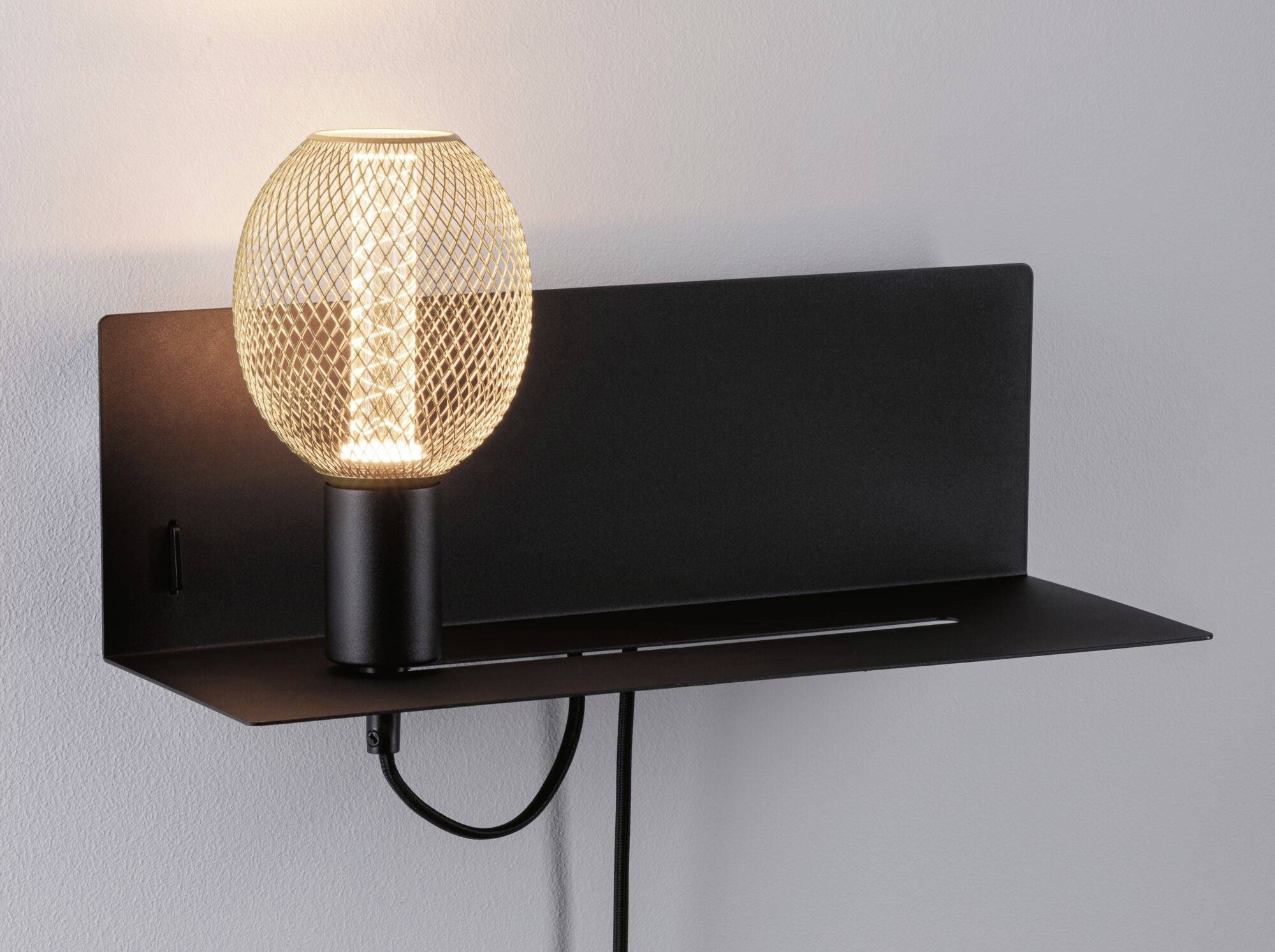 Eine moderne Wandlampe mit schwarzem Metallsockel und rundem, strukturiertem Lampenschirm, leuchtet an einer weißen Wand.