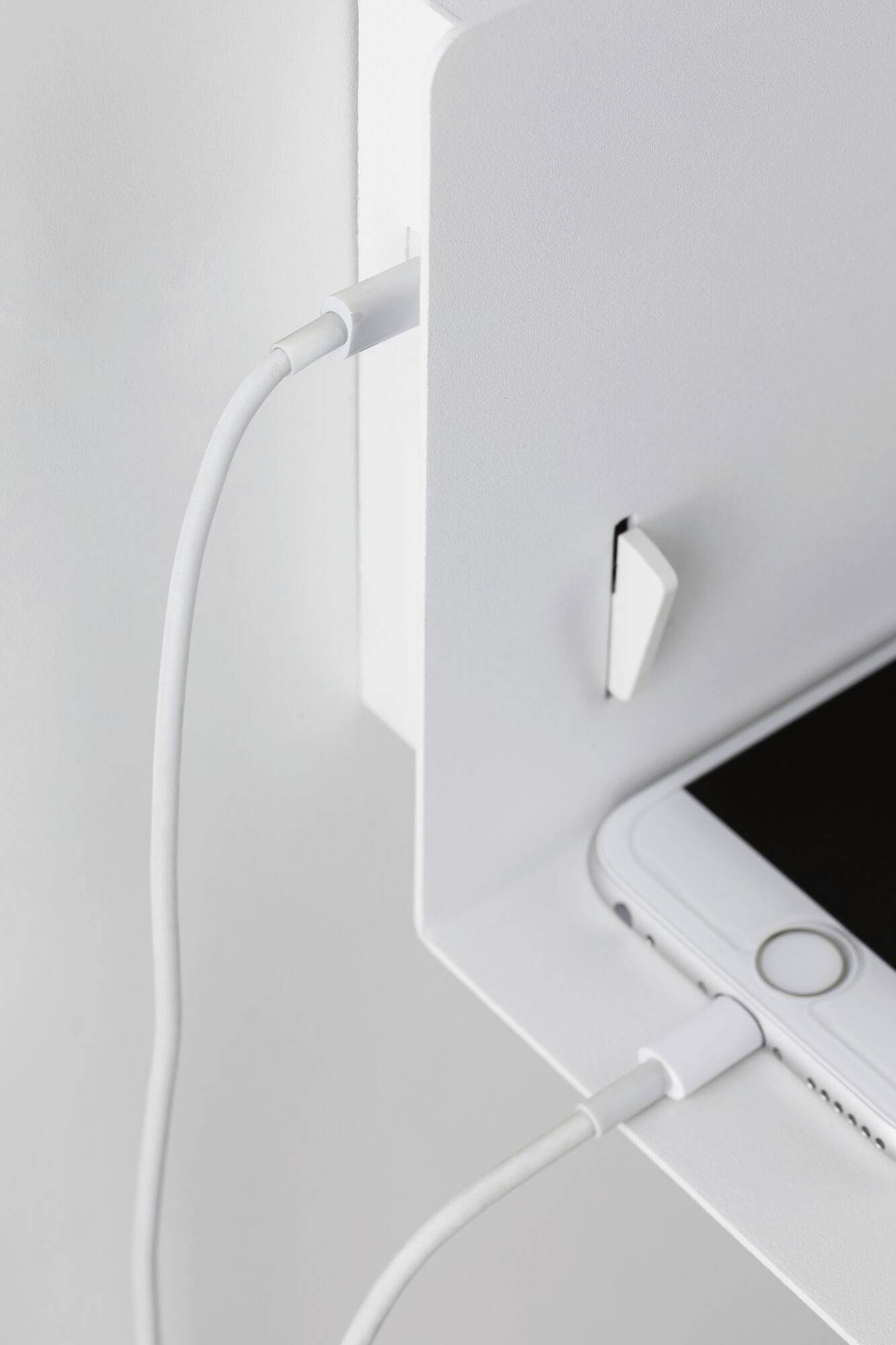 Ein Smartphone lädt auf einer weißen Ablage, angeschlossen durch ein weißes Ladekabel.