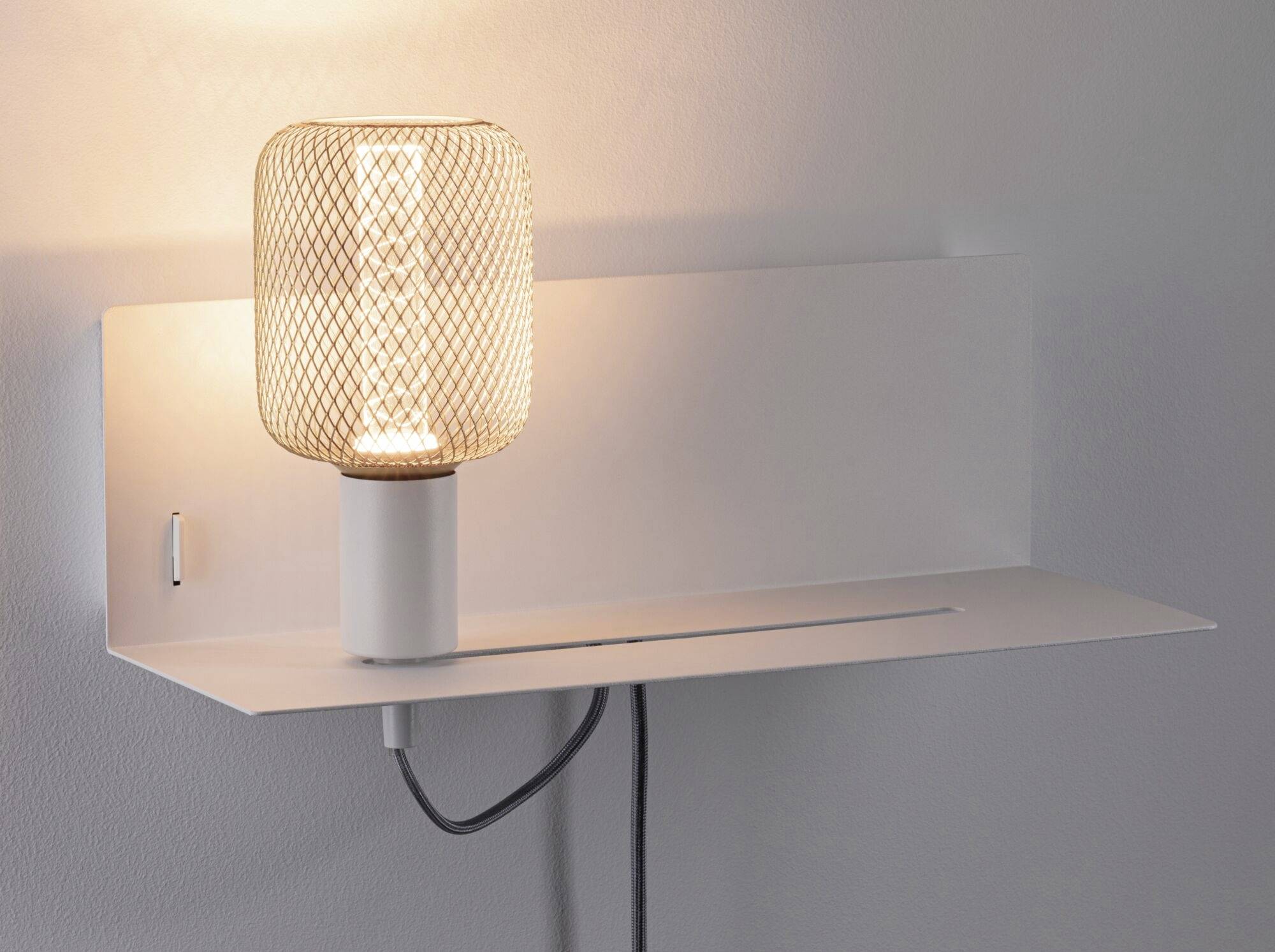 Moderne Wandleuchte mit Gitterlampenschirm und integriertem Regalbrett, strahlt warmes Licht aus, schwarzes Kabel sichtbar.