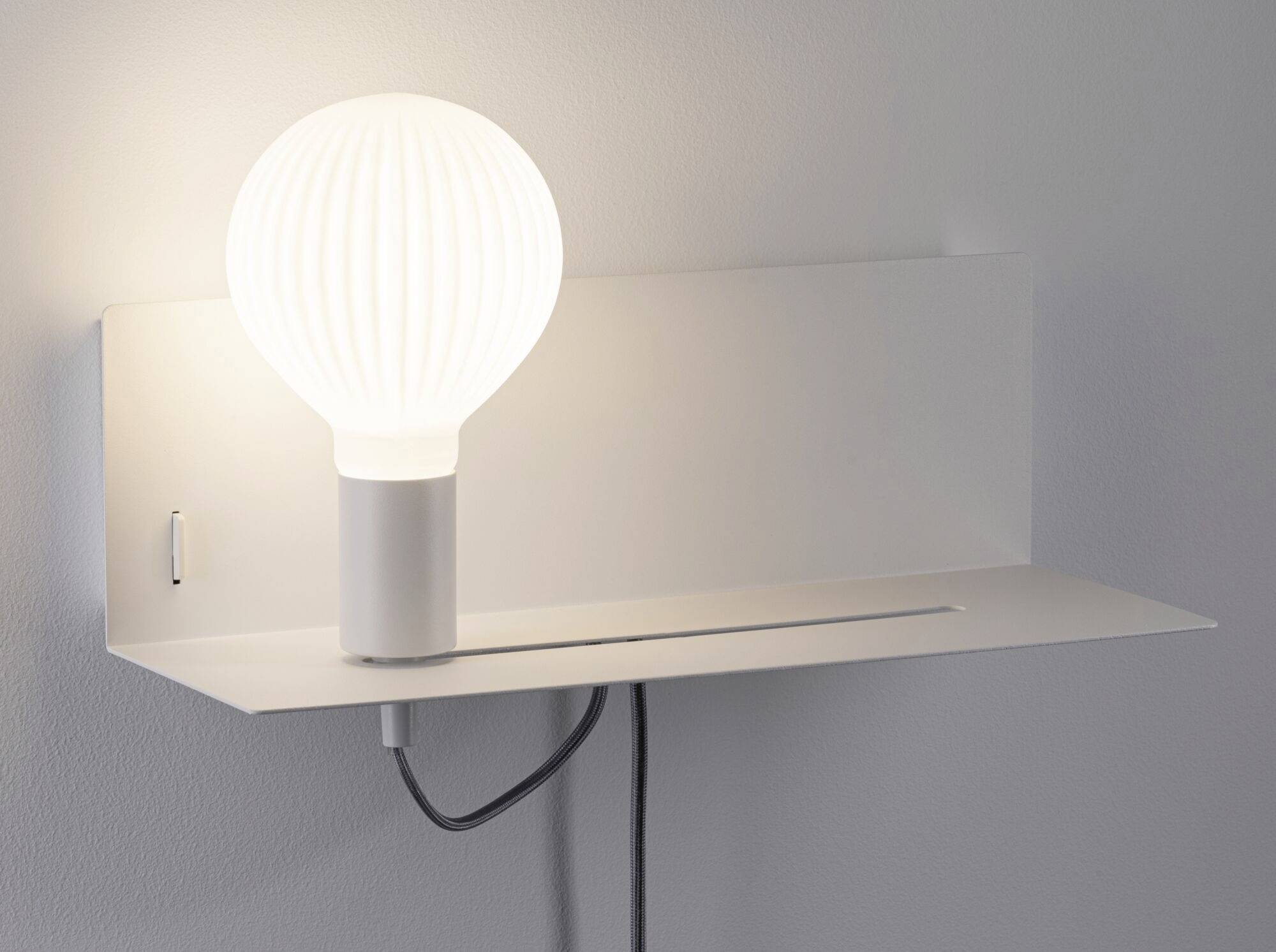 Eine moderne Wandleuchte mit weißem, geripptem Glas und schwarzem Kabel, auf einem schlichten weißen Regal montiert.