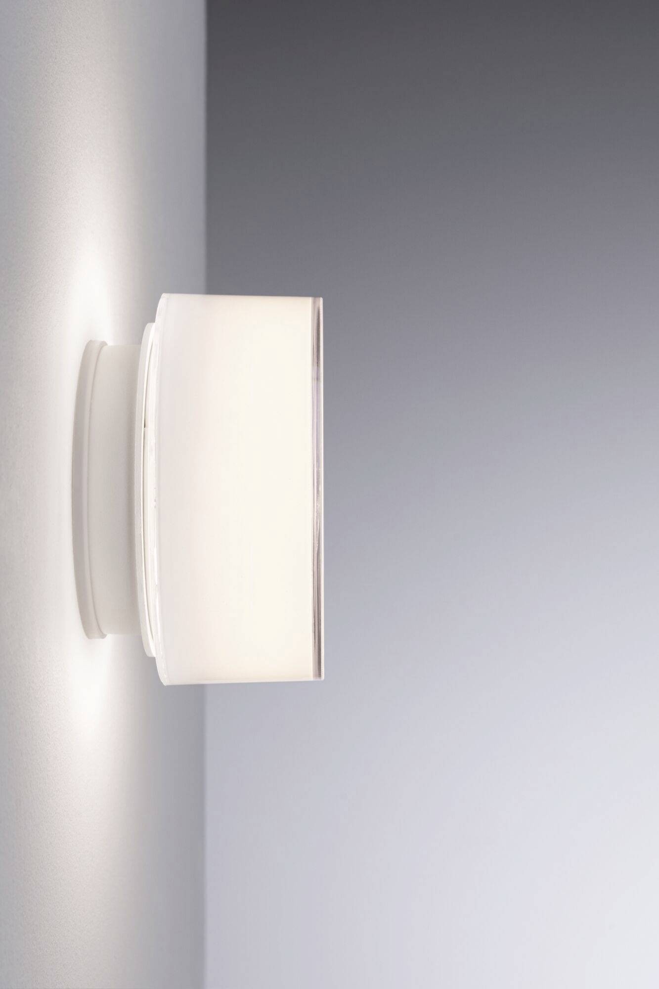 Wandleuchte mit modernem, minimalistischem Design, montiert an einer hellgrauen Wand. Leuchtet sanft nach oben und unten.