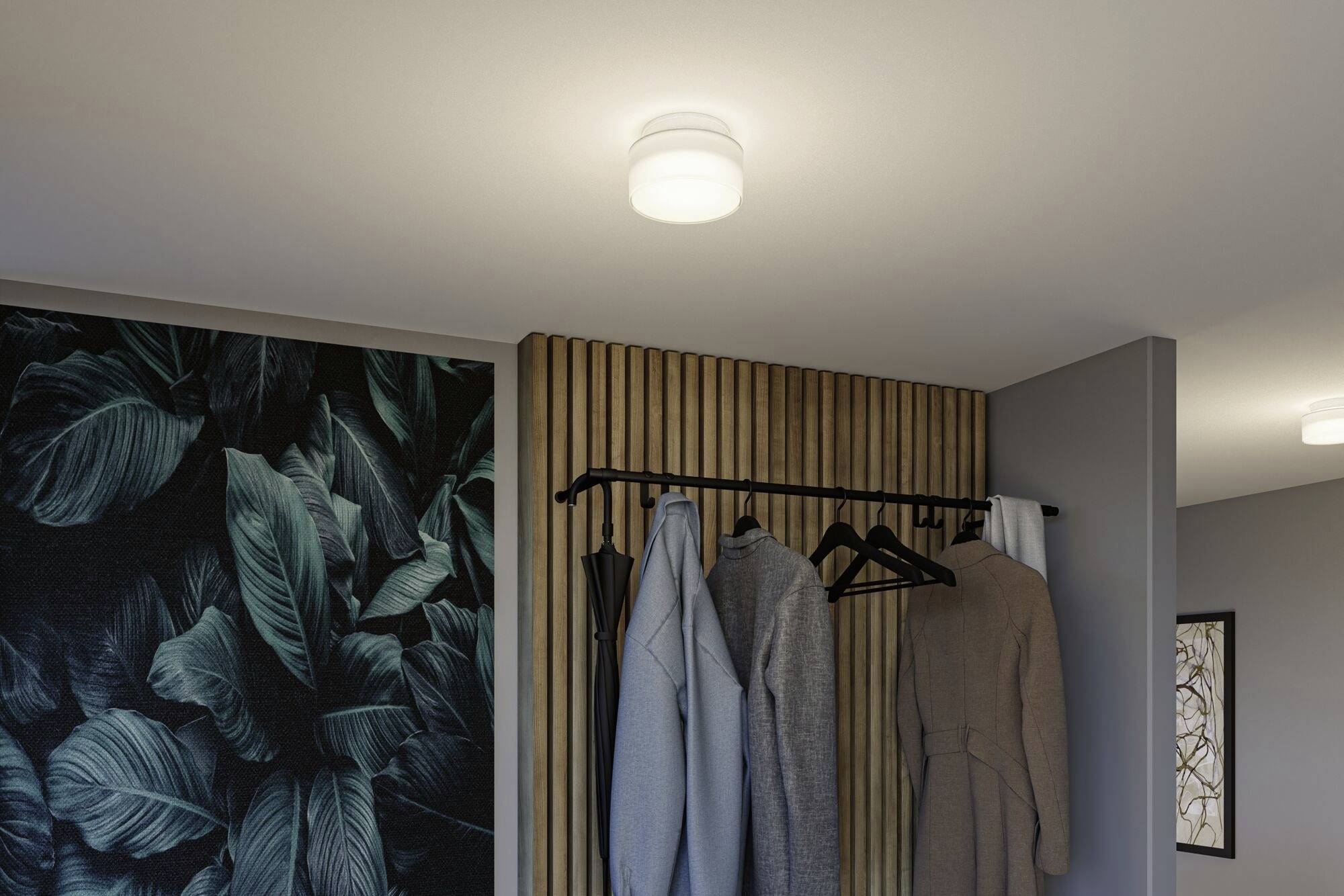Eine modern eingerichtete Garderobe mit schlichter Deckenleuchte, mehreren Mänteln an einem Kleiderständer und dekorativer Blättertapete.