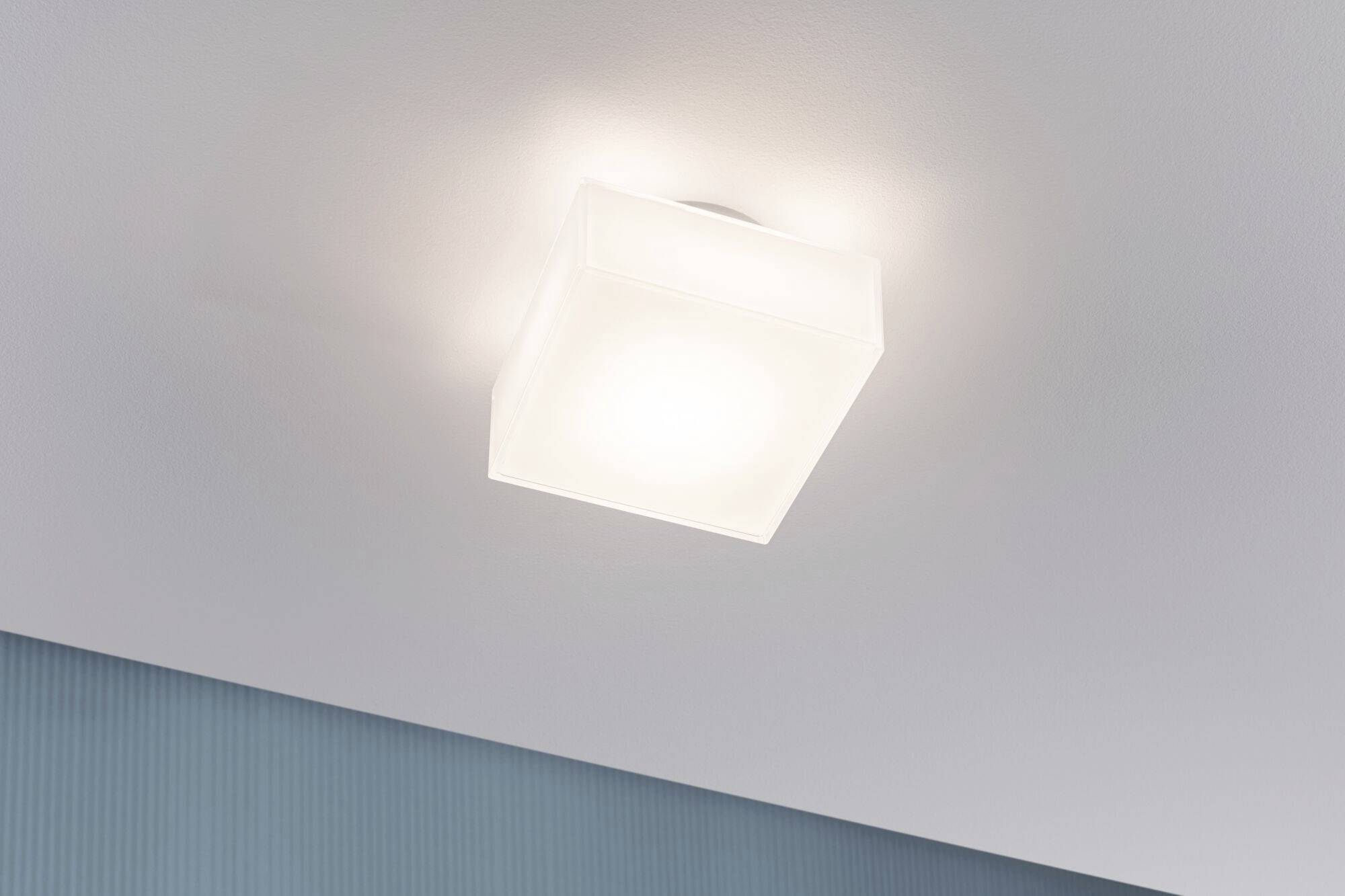 Weiße, quadratische Deckenleuchte strahlt weiches Licht aus. Darunter blauer Streifen an der Wand, moderner, minimalistischer Raum.