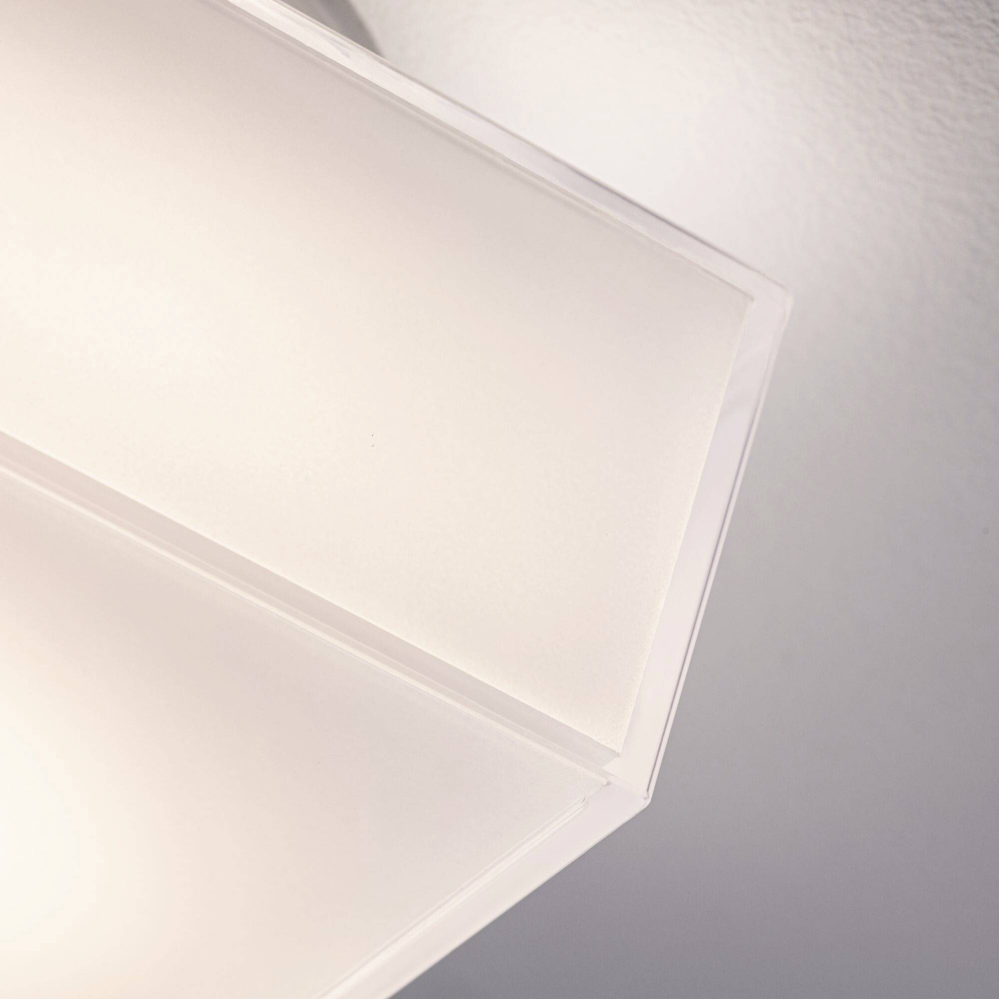 Eine moderne Deckenleuchte mit schlichter, geometrischer Form leuchtet an der weißen Decke. Sie erzeugt warmes, indirektes Licht.