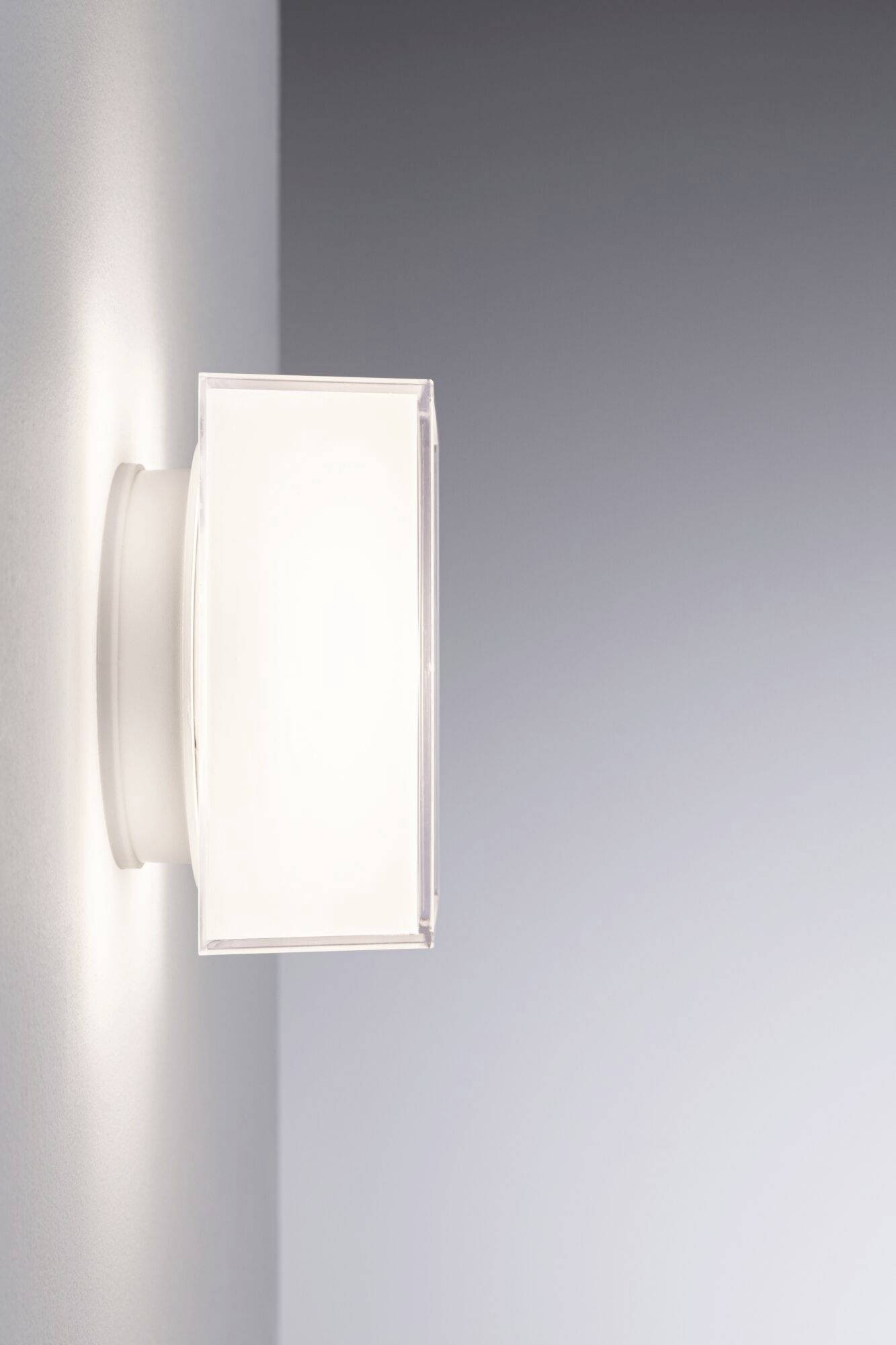 Eine rechteckige Wandleuchte mit diffusem weißem Licht, montiert an einer grauen Wand, erhellt die Umgebung sanft.