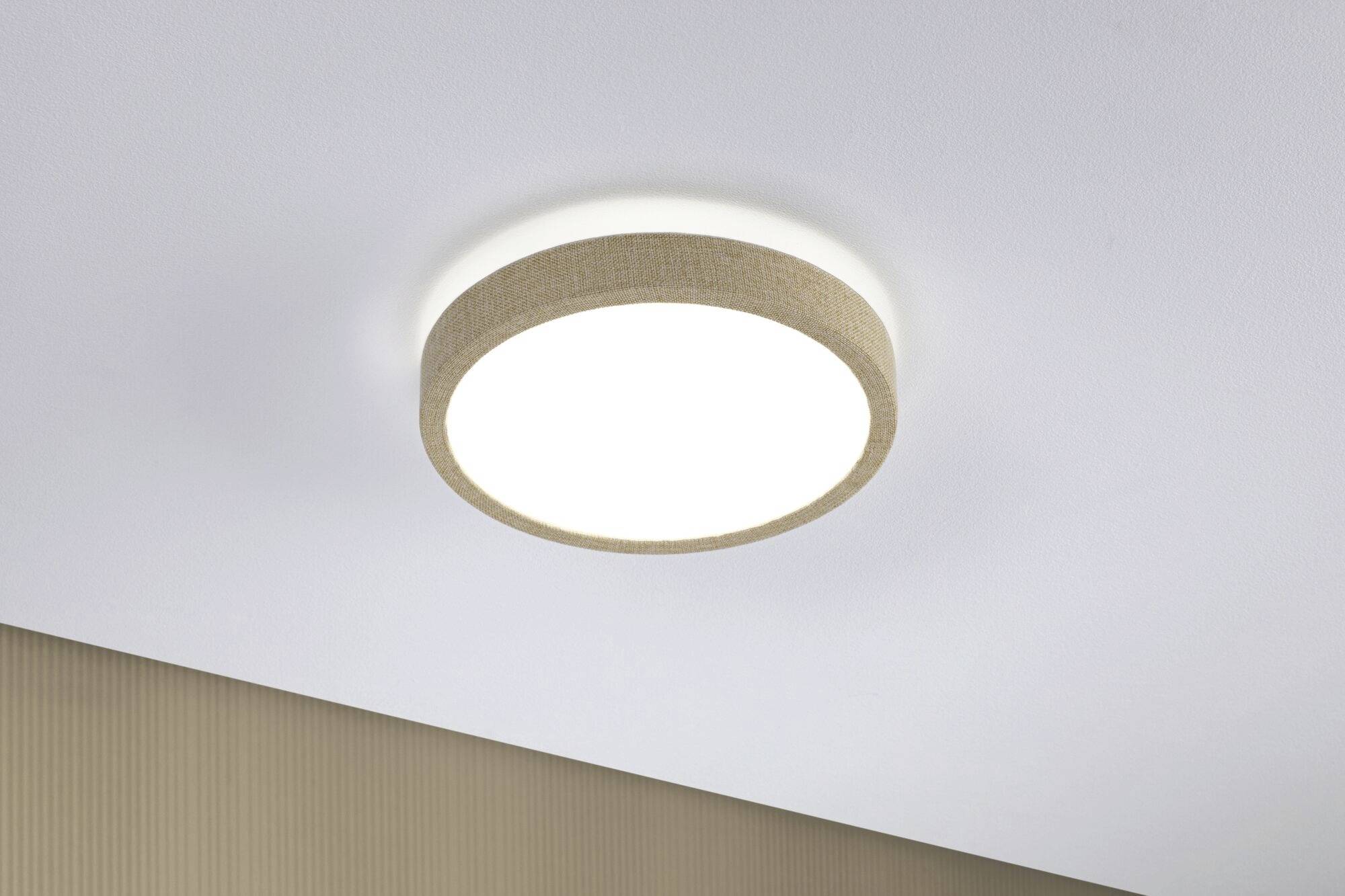 Runde Deckenleuchte mit hellem Licht, an einer weißen Decke montiert. Der Rahmen ist mit beigem Stoff verkleidet.