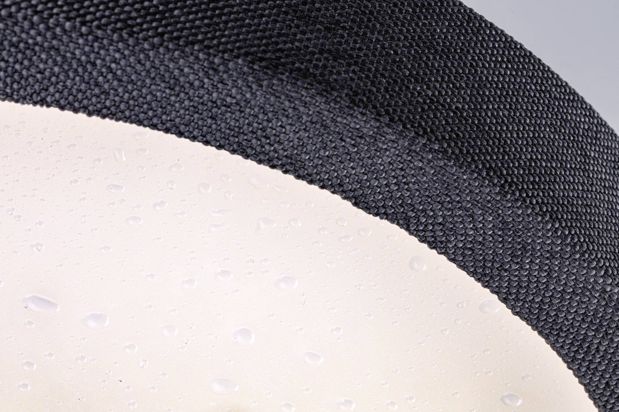 Nahaufnahme einer schwarzen, texturierten Oberfläche mit Wassertropfen auf einer glatten, beige leuchtenden Fläche daneben.