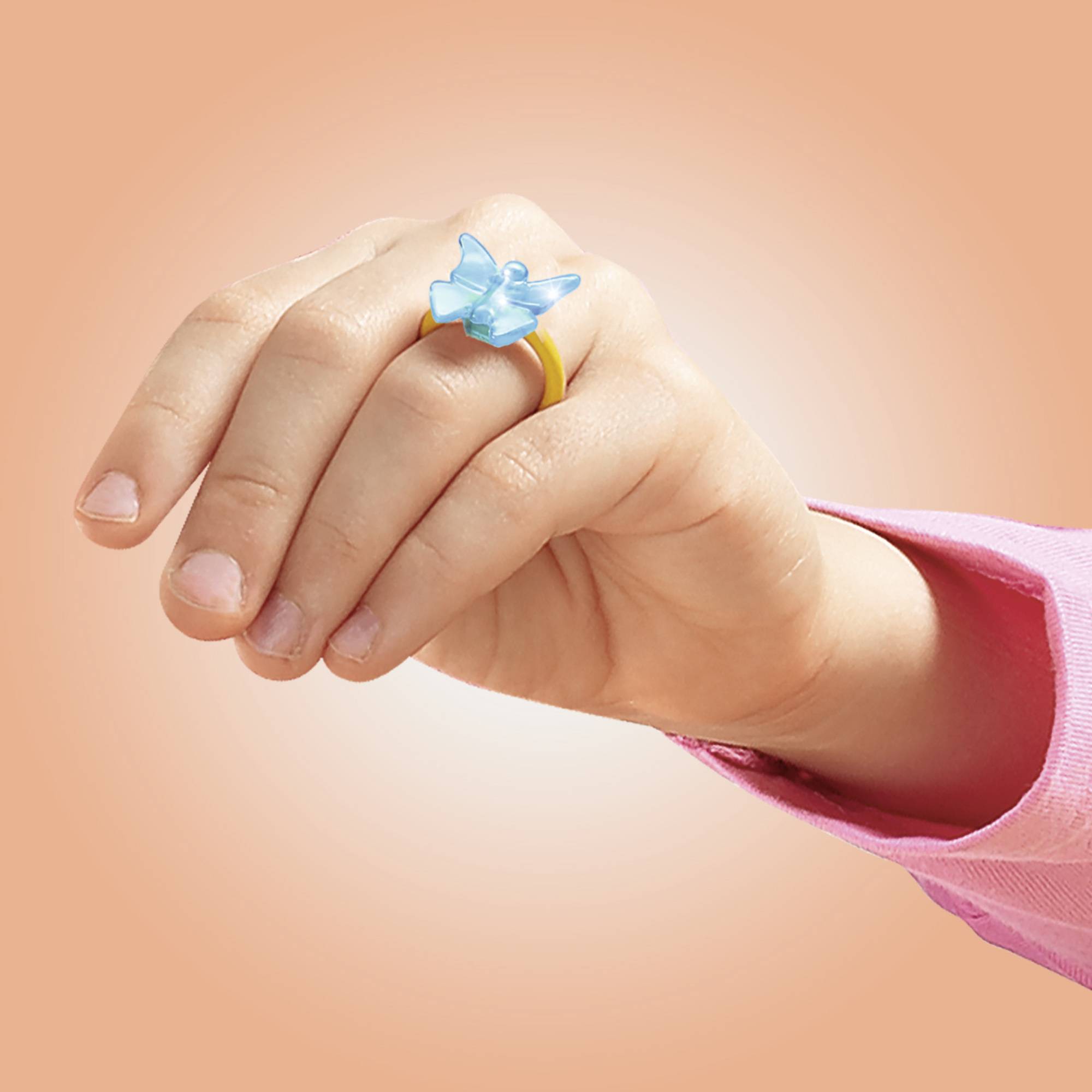 Eine Hand trägt einen gelben Ring mit einem blauen Schmetterlingsdetail. Die Hand hat eine rosa Ärmel.