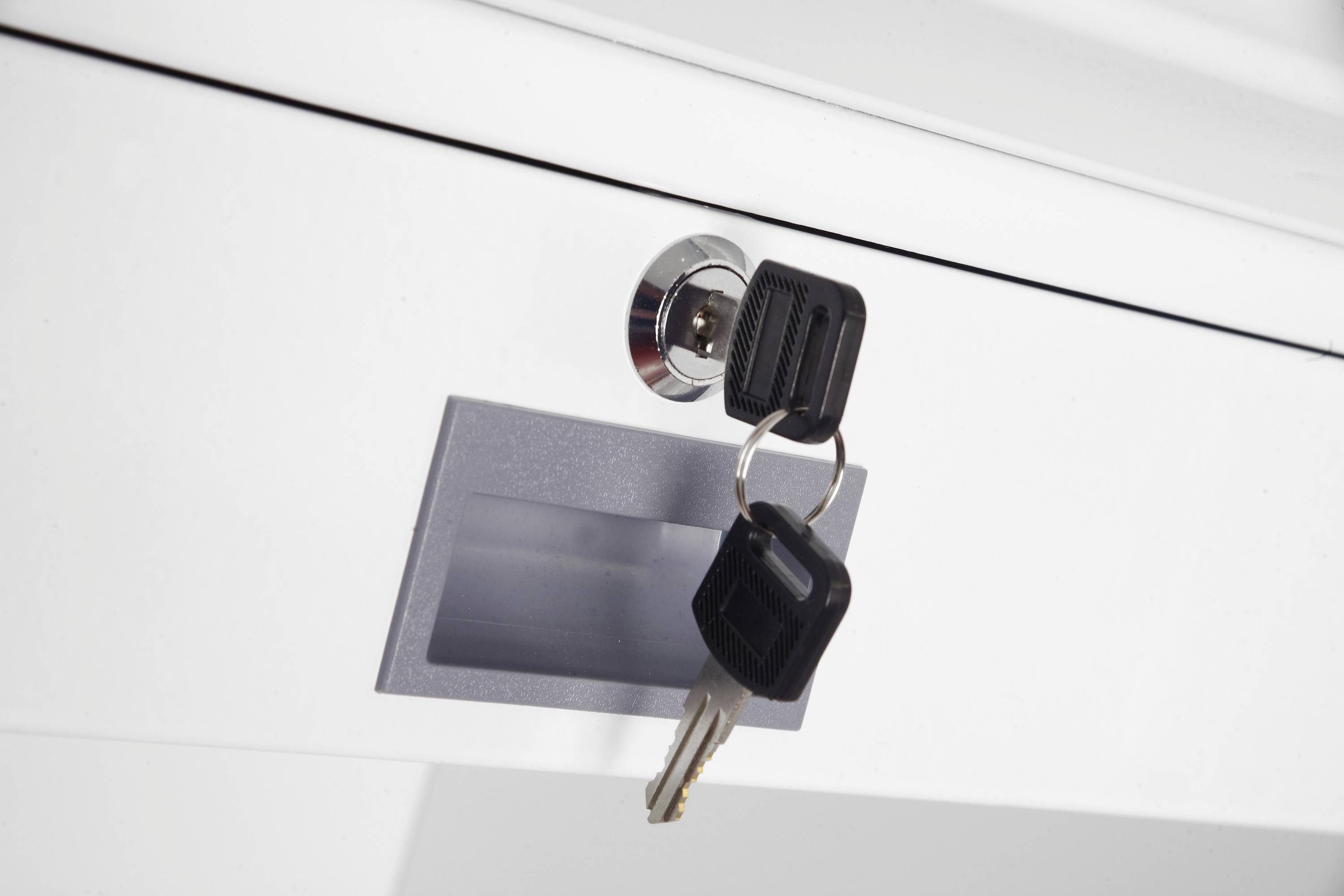 Ein Schlüsselpaar steckt in einem Schloss einer weißen Schublade. Beides hängt am gleichen Schlüsselanhänger.