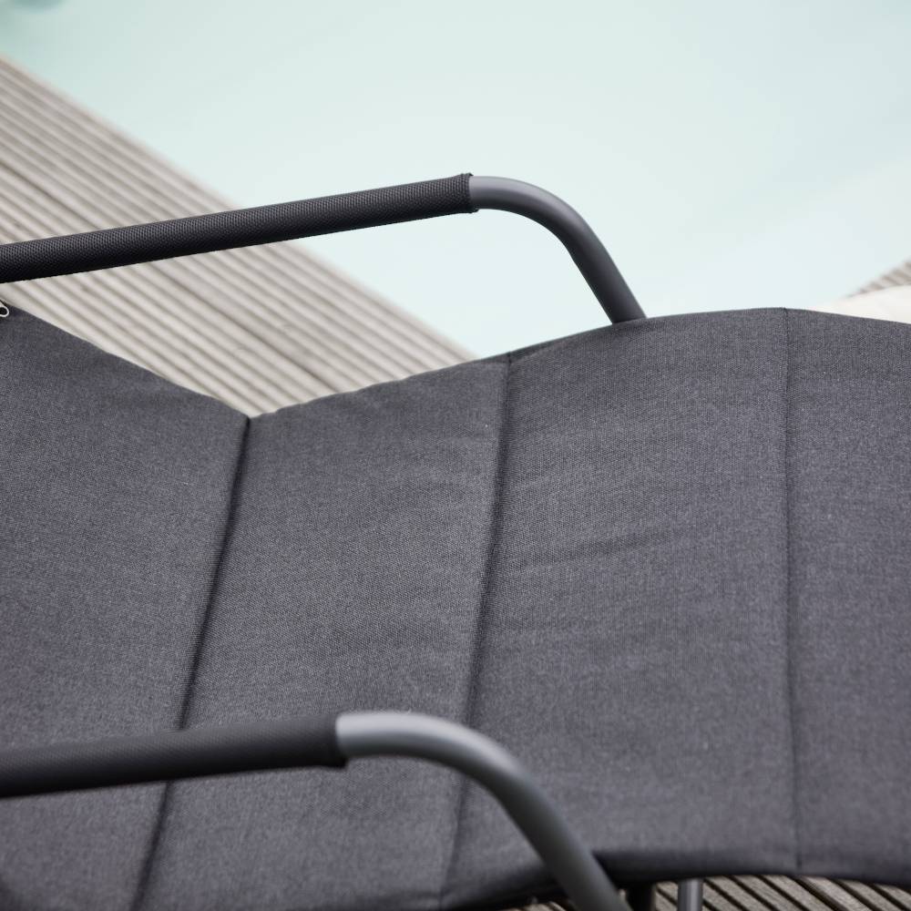 Ein Liegestuhl aus schwarzem Stoff steht auf einem Holzdeck neben einem hellblau schimmernden Pool.