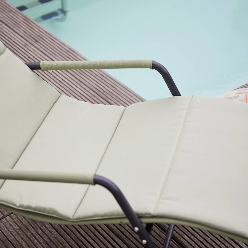 Eine grüne Sonnenliege steht auf einem hölzernen Pooldeck am Rand eines Pools.