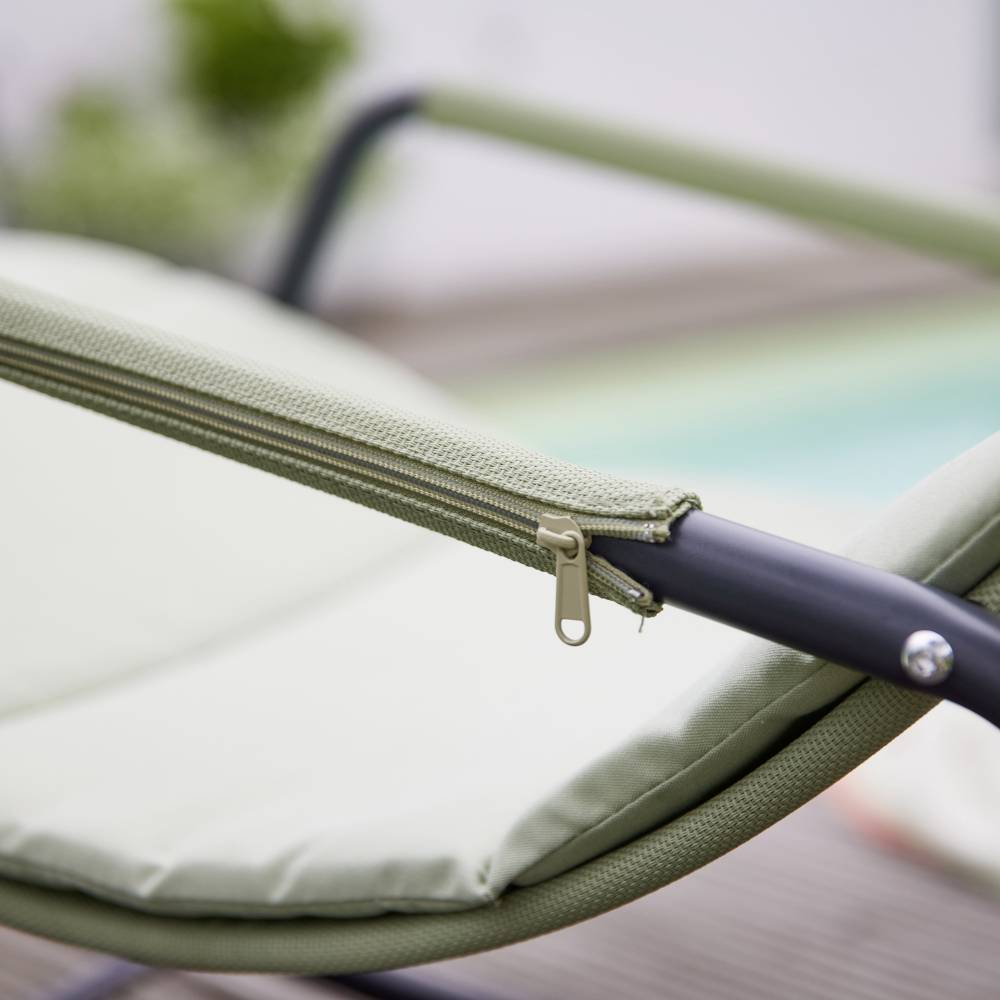 Nahaufnahme eines Outdoor-Sonnenstuhls mit grünem Stoff und schwarzem Metallrahmen vor einem verschwommenen Hintergrund.