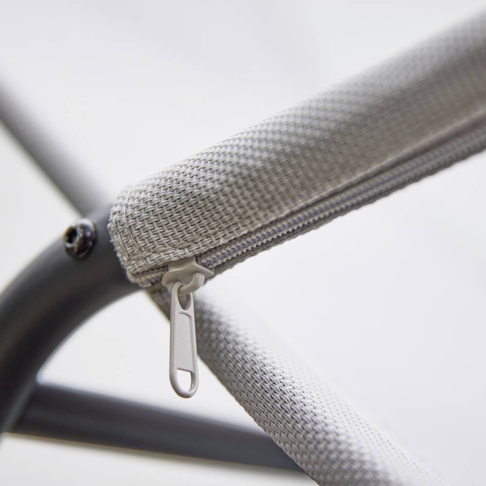 Eine Nahaufnahme eines grauen Stoffstuhls mit einem Reißverschluss an der Armlehne, auf einem Metallrahmen montiert.
