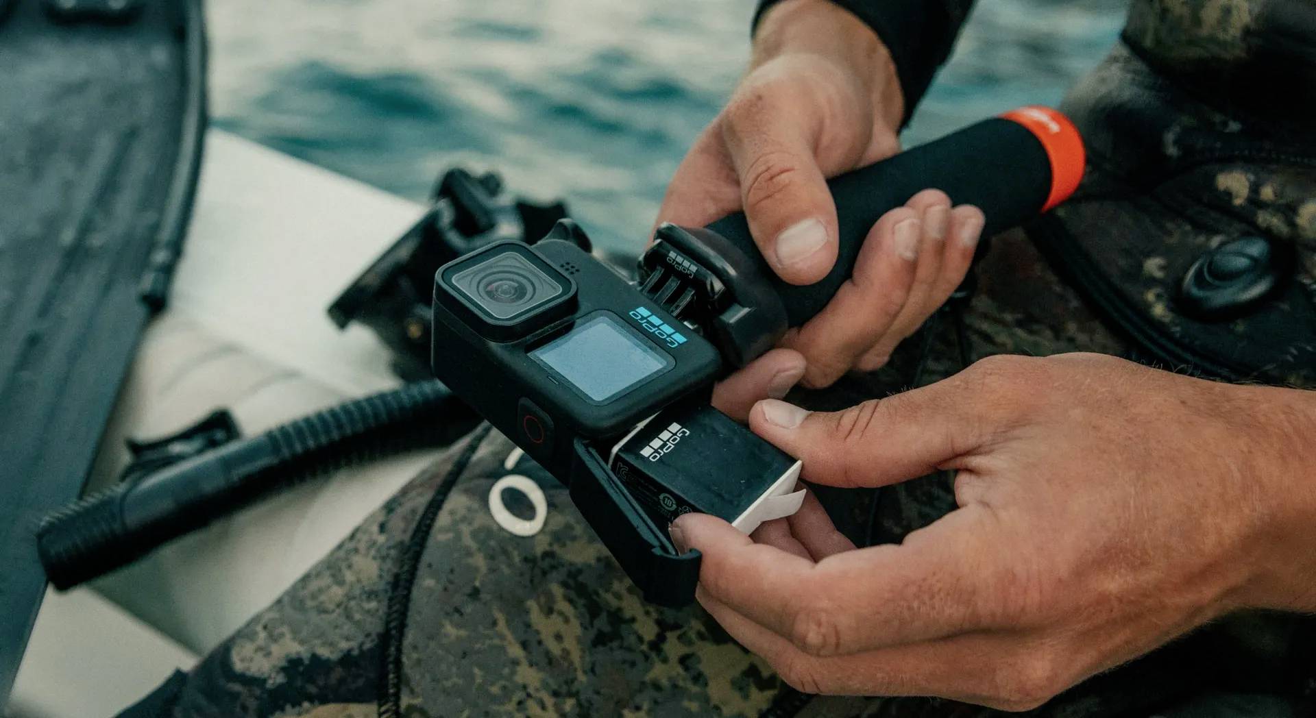 Eine Person hält eine Actionkamera und fügt eine Speicherkarte in die Kamera ein, während sie auf einem Boot sitzt.