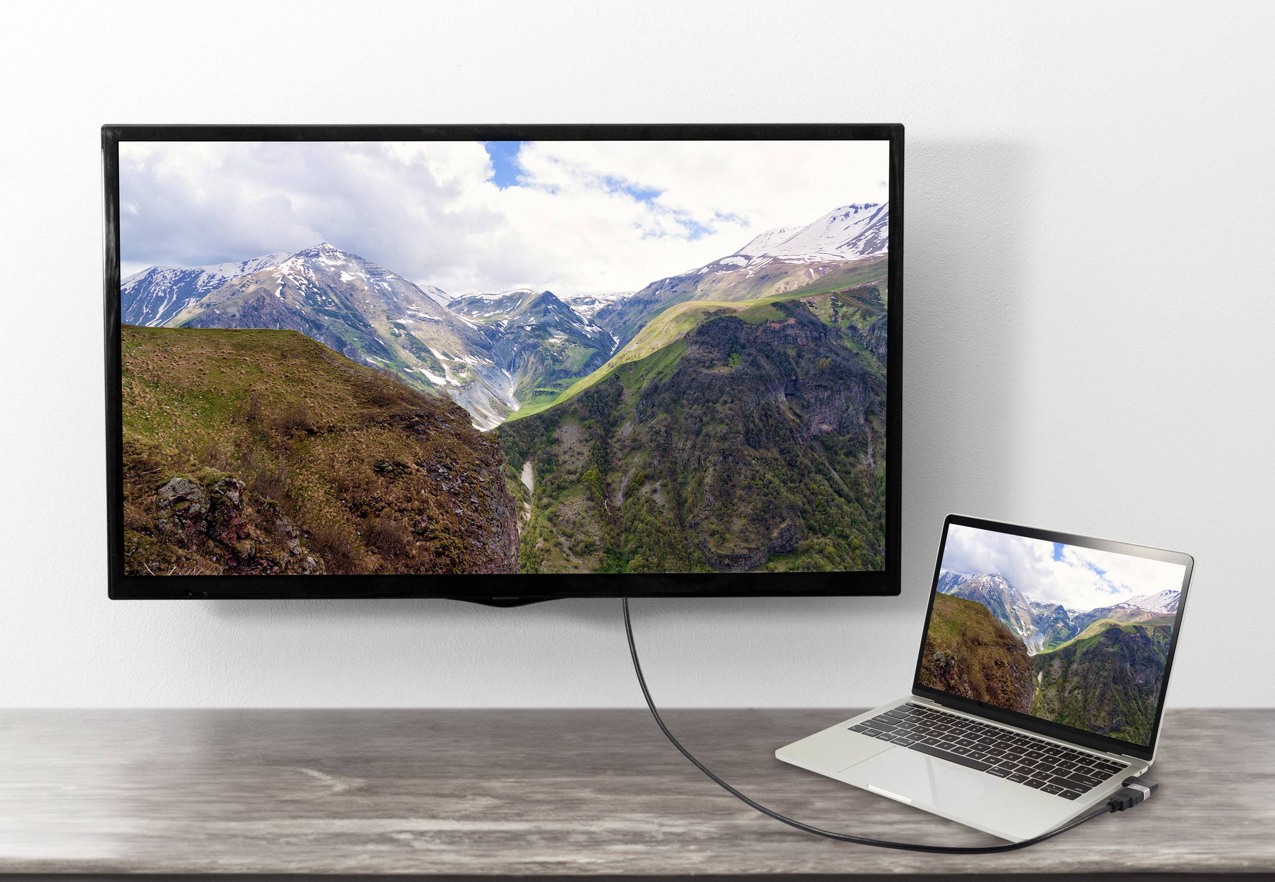 Ein Laptop ist mit einem größeren Bildschirm verbunden, der eine Landschaft mit Bergen und bewölktem Himmel zeigt.