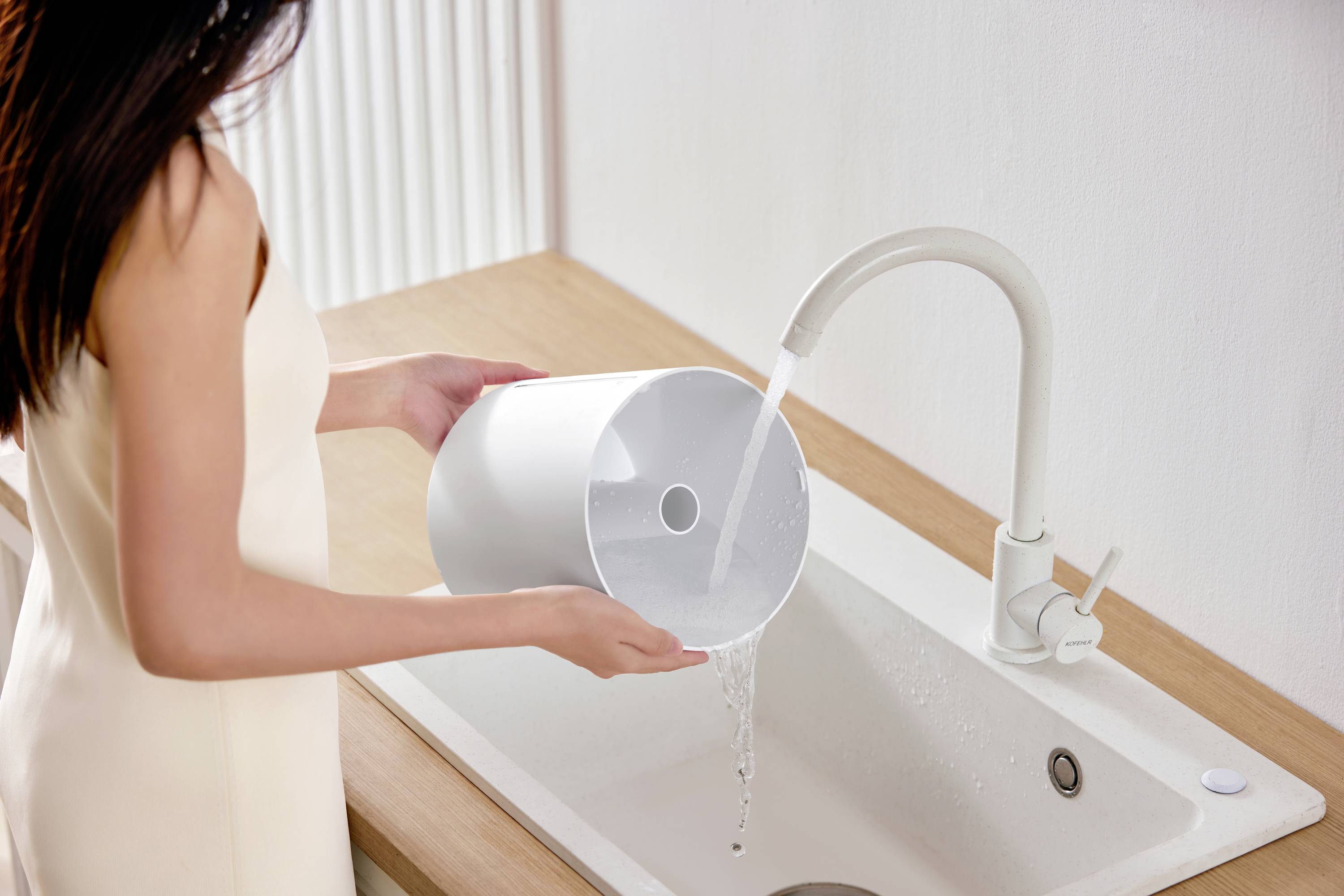 Person füllt eine weiße Karaffe am Wasserhahn an einem Waschbecken auf.