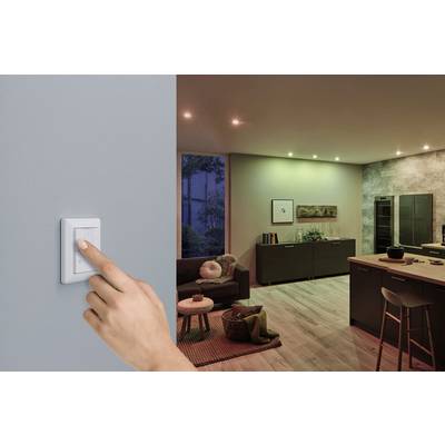 Eine Hand betätigt einen Lichtschalter an der Wand, um ein modern eingerichtetes Wohnzimmer mit gedimmtem Licht einzuschalten.