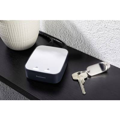 Ein Smart-Home-Steuergerät mit einem Stromkabel auf einem Tisch neben einem Blumentopf und einem Schlüsselbund.